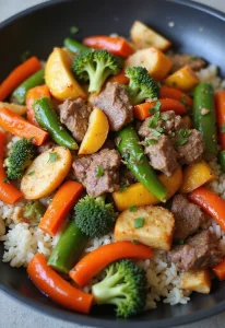 A white bowl filled with a beef stir-fry served over rice, featuring tender browned beef pieces mixed with sliced green bell peppers, orange carrots, and light green vegetables, all coated in a glossy savory sauce and garnished with chopped herbs.